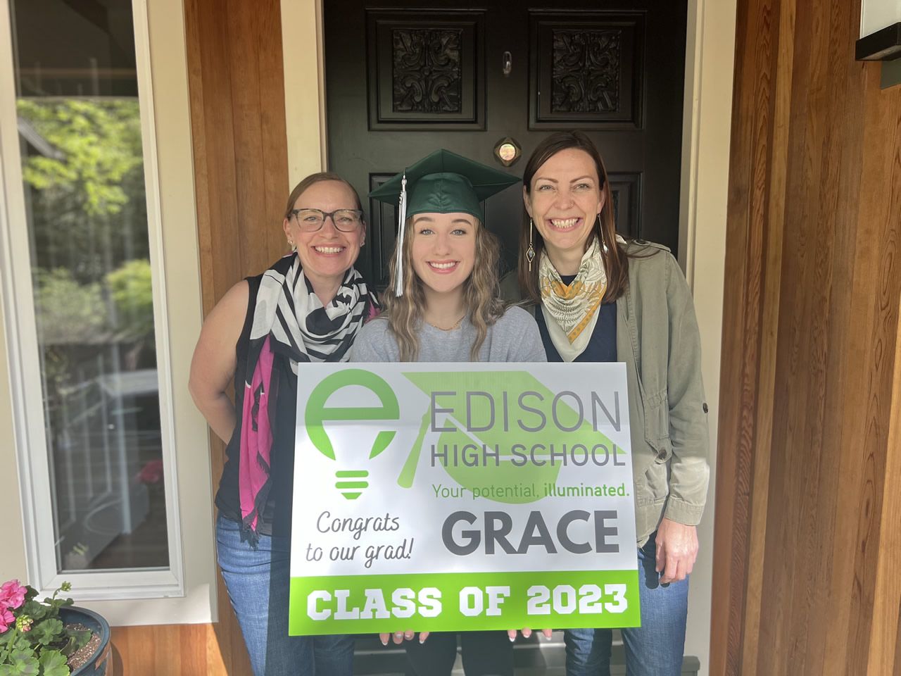 Grad smiles with her yard sign, flanked by proud Edison teachers.